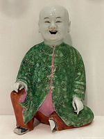 Full frontal view of the porcelain figurine showing the entire seated man with green robe and brown support.