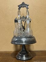 Front view of antique silver plate cruet set with five glass bottles, one decanter shows crack