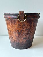 Front view of cylindrical waste paper bucket wrapped in brown leather with brass ring hardware.
