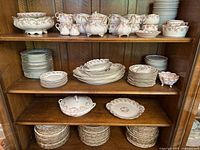 Overall view of pink and white floral porcelain dinnerware set arranged on wooden hutch