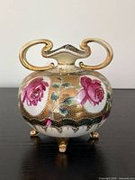 Front view of small antique Nippon porcelain floral footed vase showing hand-painted pink roses and gold-plated handles and feet.
