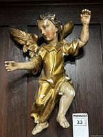 Full front view of gilt-painted angel sculpture mounted on wood panel