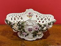 Front perspective showing applied porcelain roses, green leaves, lattice pierced sides, hand painted floral motifs, and gilding on ornate edges.