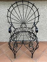 Front view of black wrought iron child’s chair showing detailed scrollwork and fan-shaped backrest.