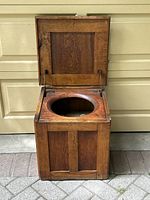 Open view of the antique wooden commode showing the hinged lid lifted and the round seat opening inside.