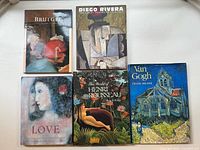 Five hardcover art books arranged on a flat surface, showing covers including Bruegel, Diego Rivera, Henri Rousseau, Van Gogh, and Love in Art Anthology.