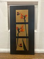 Full view of the black-framed wooden panel with three golded sections each containing orange flowers and butterflies.