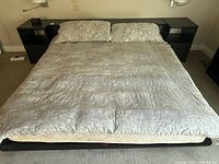 Bed made with king size grey, white, and beige patterned duvet cover and 2 pillow shams on black frame platform bed