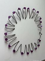 Circular avant garde necklace formed from silver toned wire with zig-zag loops and purple lucite cube beads on each loop.