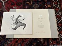 Photo showing one lithographic print with rabbit figure holding a clock and pen, portfolio folder partially visible underneath