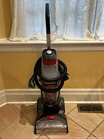 Front view of the upright carpet cleaner showing overall design and coiled hose.