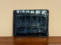 Front exterior side of the black crocodile leather wallet showing rectangular scale pattern and some scuff marks.