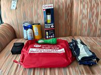 Full lot on couch: red Joxar first aid kit, Fox 40 fire extinguisher in box, OR black/white boating gloves, black case