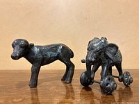 Pair of bronze animal sculptures on wooden surface, showing a standing calf and a detailed elephant on wheels.
