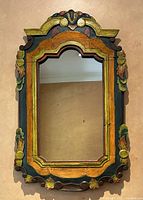 Full frontal view of the hand painted carved wood framed mirror hanging on a wall showing detailed shape and color.