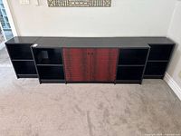 Front view of contemporary style black credenza with five sections, featuring red-toned double cabinet doors in the center and open shelving units on either side.