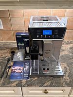 Front view of machine with milk carafe on left, accessories (box, manual, filter cartridges, cleaning tools) arranged in front.