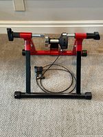Front view showing the red and black stationary trainer stand with resistance unit in center.