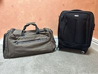 Eddie Bauer olive green duffel bag alongside black Samsonite rolling carry-on suitcase on carpeted floor.