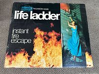Box front featuring American LaFrance brand and Life Ladder logo, showing instant fire escape design with flames and descending woman.