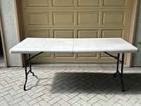 Full view of the folding table showing its length and white plastic top with black legs in outdoor setting.