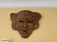 Front view of the hand made red clay decorative hanging mask showing detailed facial features and textured headdress.
