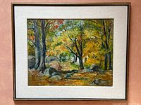 Framed oil painting showing full autumn forest landscape with trees, rocks, and fall colors in a gold frame and cream mat.