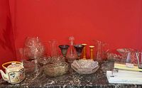Wide view of assorted glassware, crystal bowls, pitchers, and a porcelain teapot on a marble top surface against a red wall