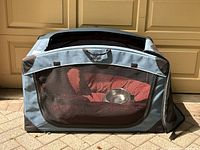 Front view of large soft sided fabric dog crate with mesh zipper panel, red dog bed and silver metal dog bowl inside.