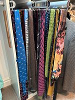 Photo showing 12 men's silk ties hanging on a rack in assorted colors and patterns including browns, blues, greens, pinks, and multi-colored artistic prints.