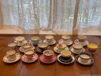 Wide view of 14 assorted English china cups and saucers on wooden table, showing variety of floral and decorative patterns
