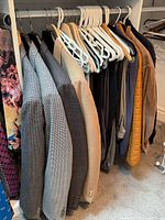 Photo showing a rack of men's clothing including blazers, jackets, and pants on hangers.