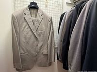 Photo showing beige/light grey wool blazer hanging next to other blazers and suits, illustrating the collection's neutral colors and mixed sizes.