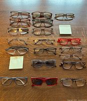 Top view of 26 mixed reading and prescription eyeglasses arranged in rows, showing a variety of frame styles and colors including brown tortoise, black, red, and patterned designs. Notes show lens magnifications 1.50, 1.75, 2.25, and 2.50.