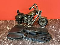 Photo showing black leather gloves and motorcycle sculpture on marble surface against red background, highlighting details of gloves and sculpture