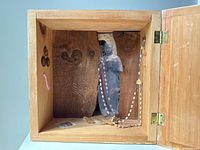Open wooden box showing interior diorama with transparent photograph of a female figure and a rosary hanging inside.