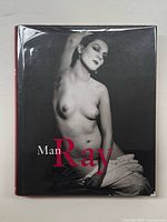 Front cover of the book showing black and white photo of a nude woman with title Man Ray in red and white text, dust jacket in good condition with minor edge wear.