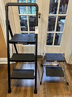 Mastercraft three-tier step ladder alongside a smaller Polder two-step ladder against a glass door on wood floor.