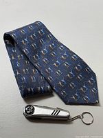 Dark blue golf-themed tie showing repeating golfer pattern, laid flat with multi-tool keychain lying on top.