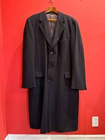 Full front view of black cashmere overcoat on hanger against red background
