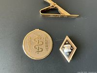Tie bar, Medic Alert pendant and enamel lapel pin displayed on dark background.