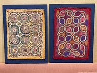 Two embroidered textile panels mounted on blue boards side-by-side, showing overall design and color, to illustrate the lot's content.