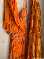 Orange beaded asymmetrical silk dress paired with matching polka dot silk scarf with beadwork, hanging on hanger
