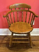 Front view of one antique Windsor armchair against red wall and hardwood flooring.