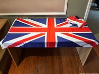 British Union Jack nylon flag spread on table showing full design, some wrinkles and stains visible, with metal grommets on the left edge.