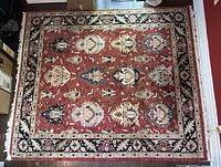 Full view of rectangular Persian style area rug with red center field and black border, showing traditional floral and geometric patterns.