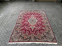 Top view of the Persian style machine-made carpet laid on pavement, showing overall design, colors, and white fringed edges.