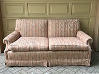Front view of the pink patterned two-seater sofa, showing rolled arms, pleated skirt and two seat cushions.