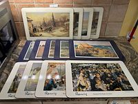 Photo showing all 13 placemats arranged fanned out on a countertop with visible prints of artworks including Renoir and Monet.