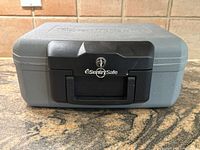 Front view of closed SentrySafe fireproof safe with key in lock on black latch, gray body, embossed logo on lid.